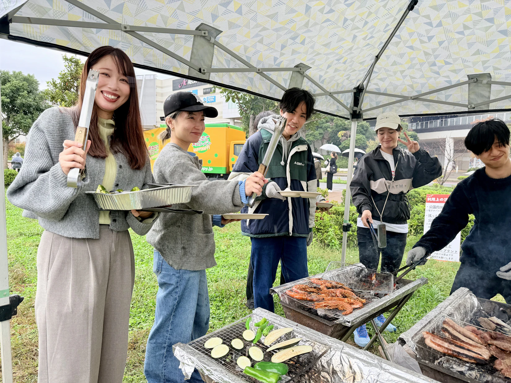 5人で楽しそうに3つのコンロを囲んでいる。それぞれコンロの上には野菜、エビ、ソーセージが載っている。