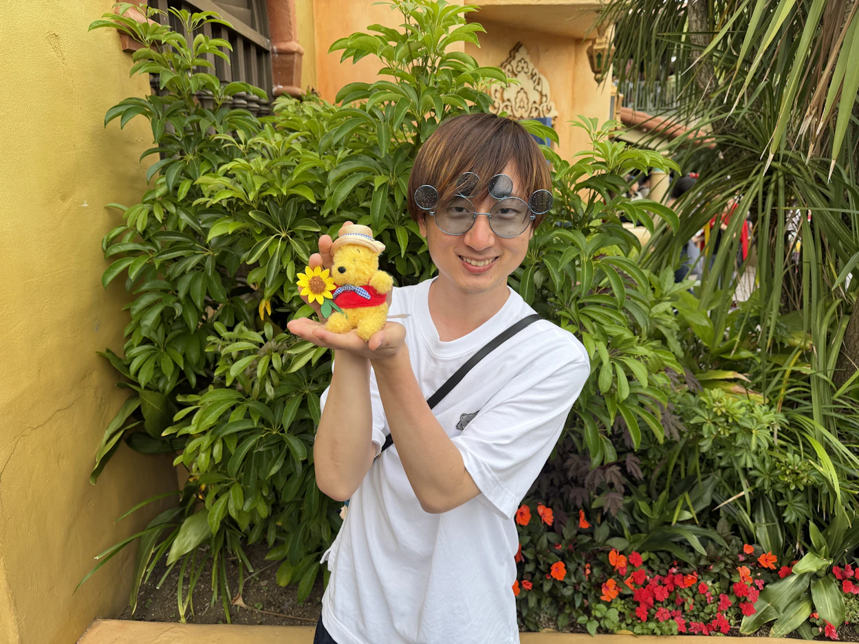 プーさんの人形を手のひらにのせている笑顔の男性社員の写真。