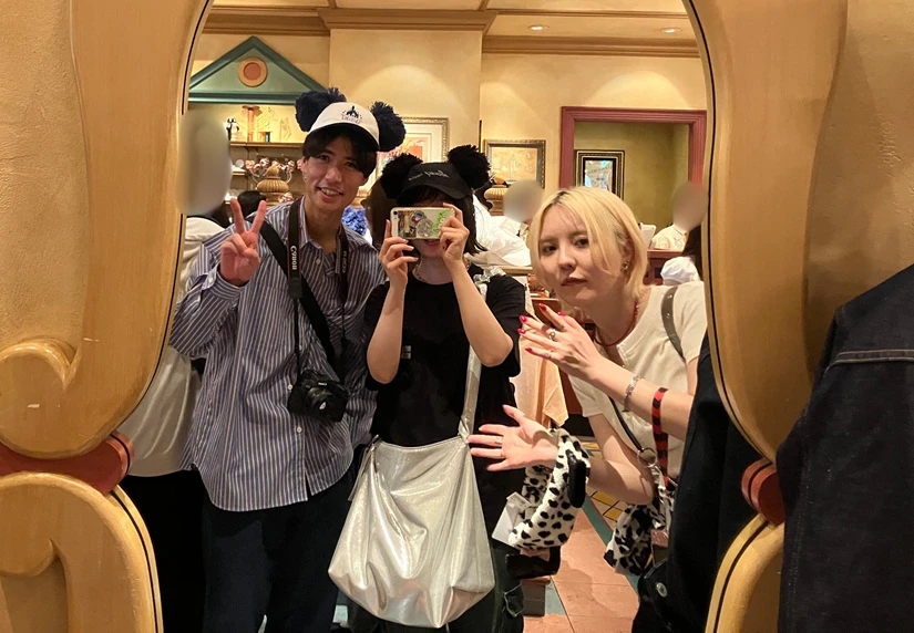 東京ディズニーシー園内のショップにて、身に着けグッズを選んでいる様子の写真。ミッキーの耳がついたキャップや、キャラクターモチーフのバンダナを手に鏡越しの記念撮影。
