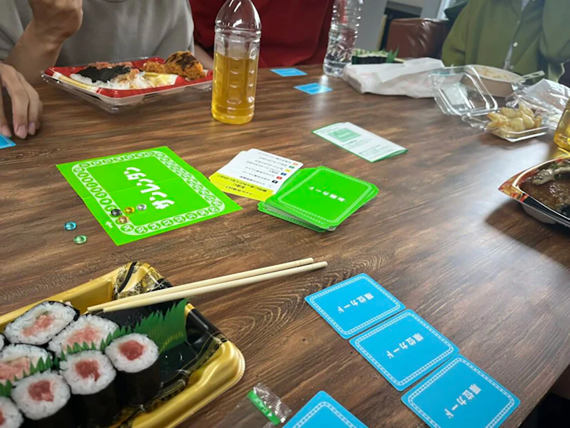 昼食をとりながらボードゲームを行うノベルティ社員。