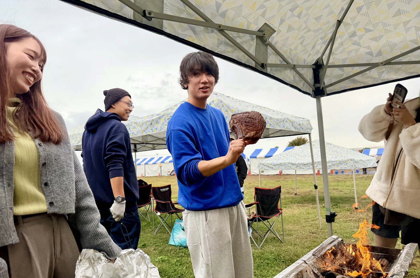 特大骨付き肉を持ってカメラに向かってポーズを決める人。後ろにはニコニコのスタッフさんも。