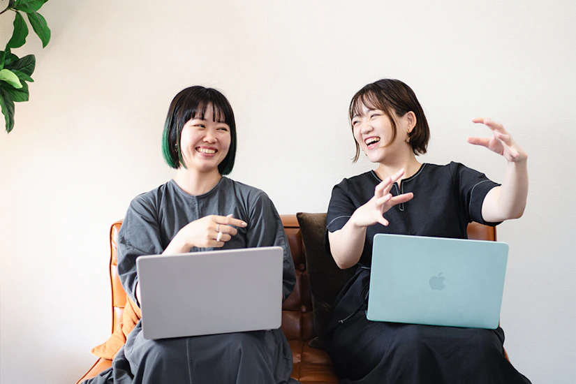 ノートPCを膝に乗せ、笑顔で会話する2人の女性。