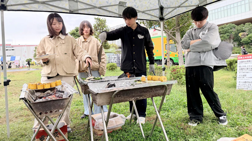 右の2人が火おこしを担当し、左の2人がコンロの上の網に切ったとうもろこしを置いている。
