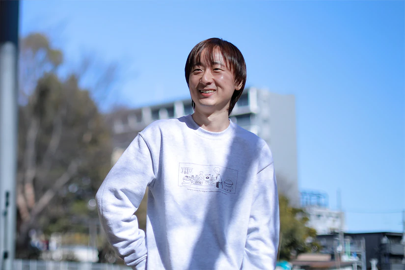 青空の下、屋外で笑顔を見せる男性。