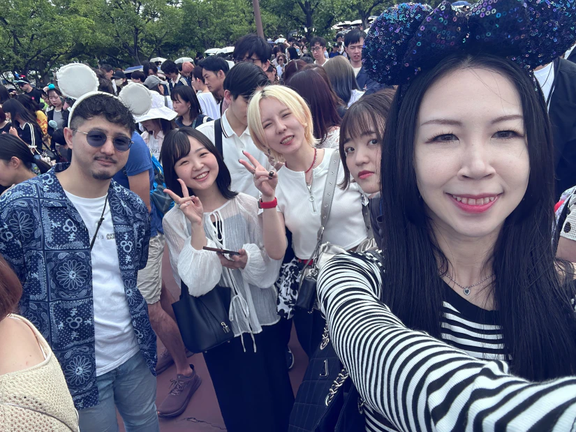 東京ディズニーシーのエントランスで、開園を待っているノベルティ社員と社長の自撮り写真。多くの人が並んでいるものの、笑顔で写真に写っている。