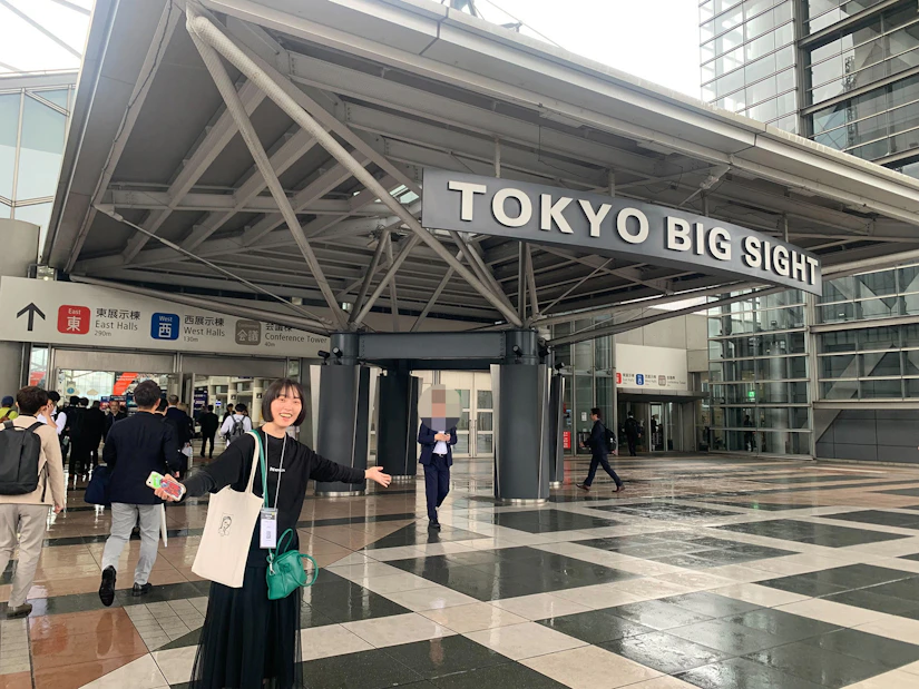 東京ビッグサイトの入り口前で、手を広げて立つノベルティ女性社員。