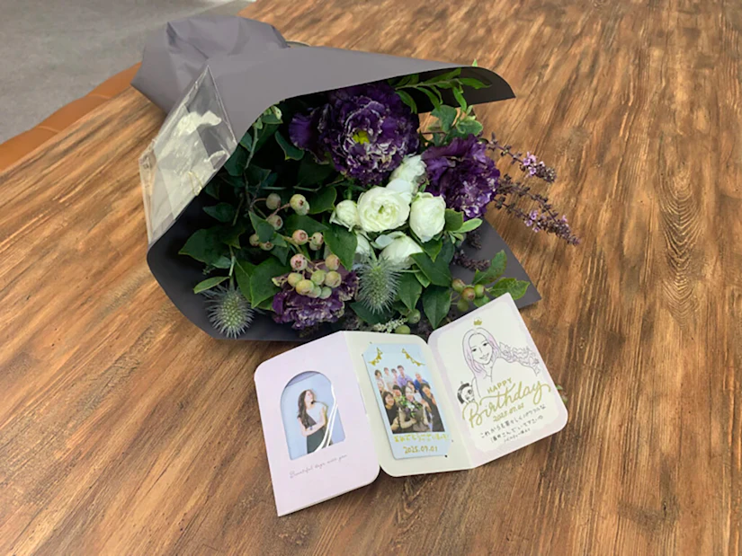 紫と白を基調とした花束と、ノベルティ代表の酒井宛のメッセージカードが机の上に置かれている。
