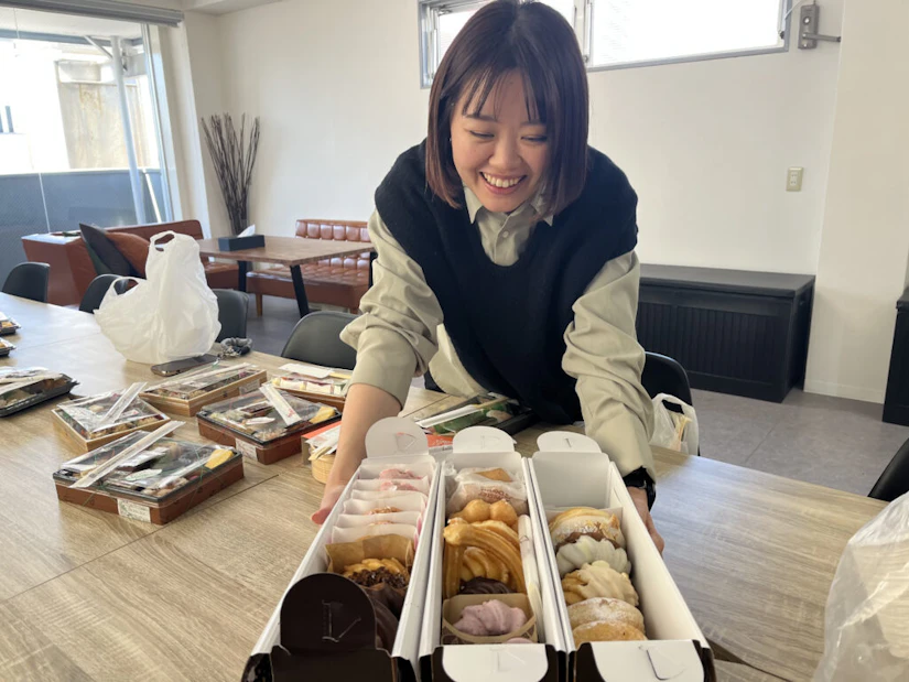 3つの箱にたくさん入ったドーナツを前に、満面の笑みを浮かべる女性。