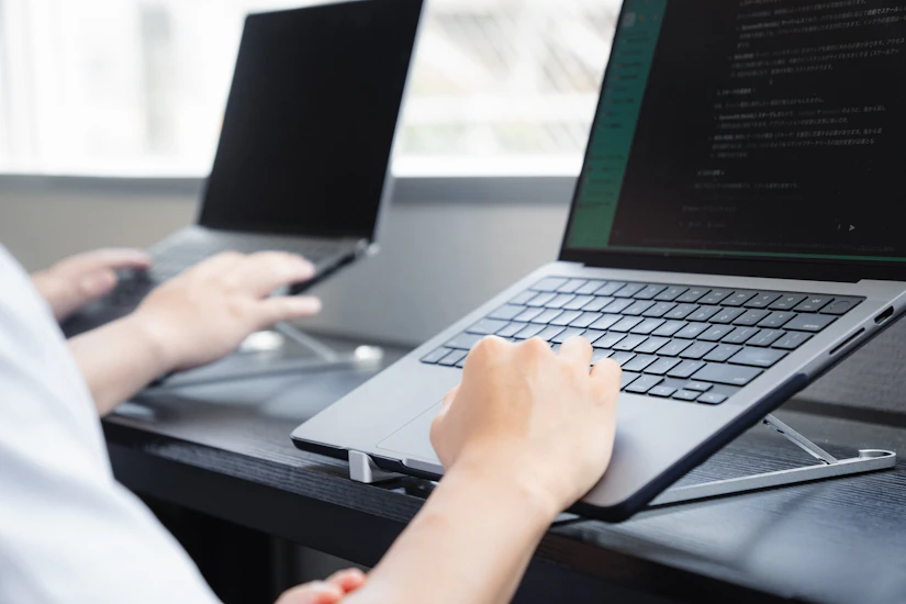ノートパソコンスタンドに置かれたPCでコードを書くエンジニアの手元。