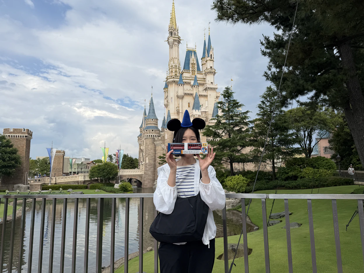 シンデレラ城の前でお土産を掲げる社員の写真。