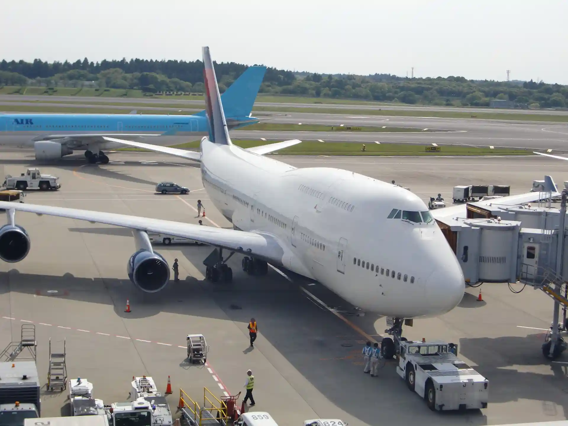 Passenger aircraft parked at a boarding gate at Narita Airport with ground crew nearby