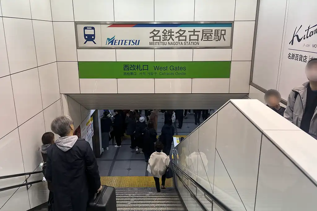 Entrance to Meitetsu Nagoya Station with signs for the West Gates and an escalator leading down to the ticket area