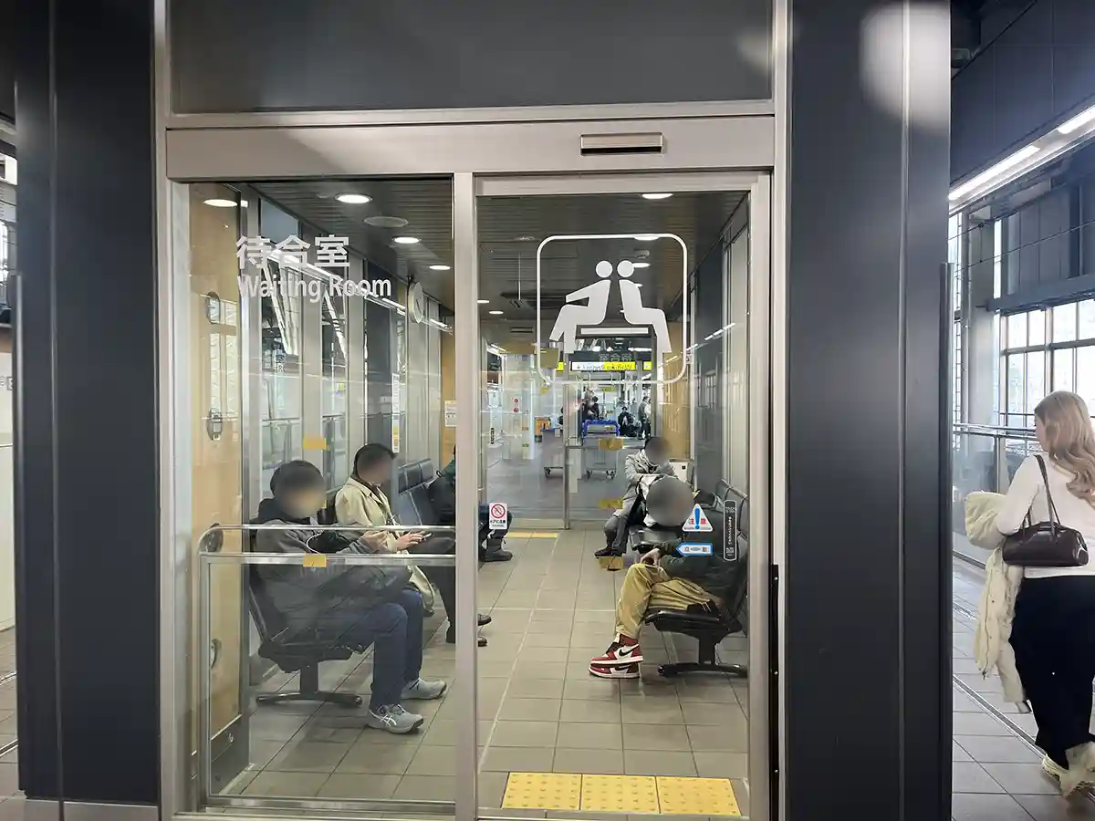 Shinkansen waiting room on the platform at Kanazawa Station with seated passengers.