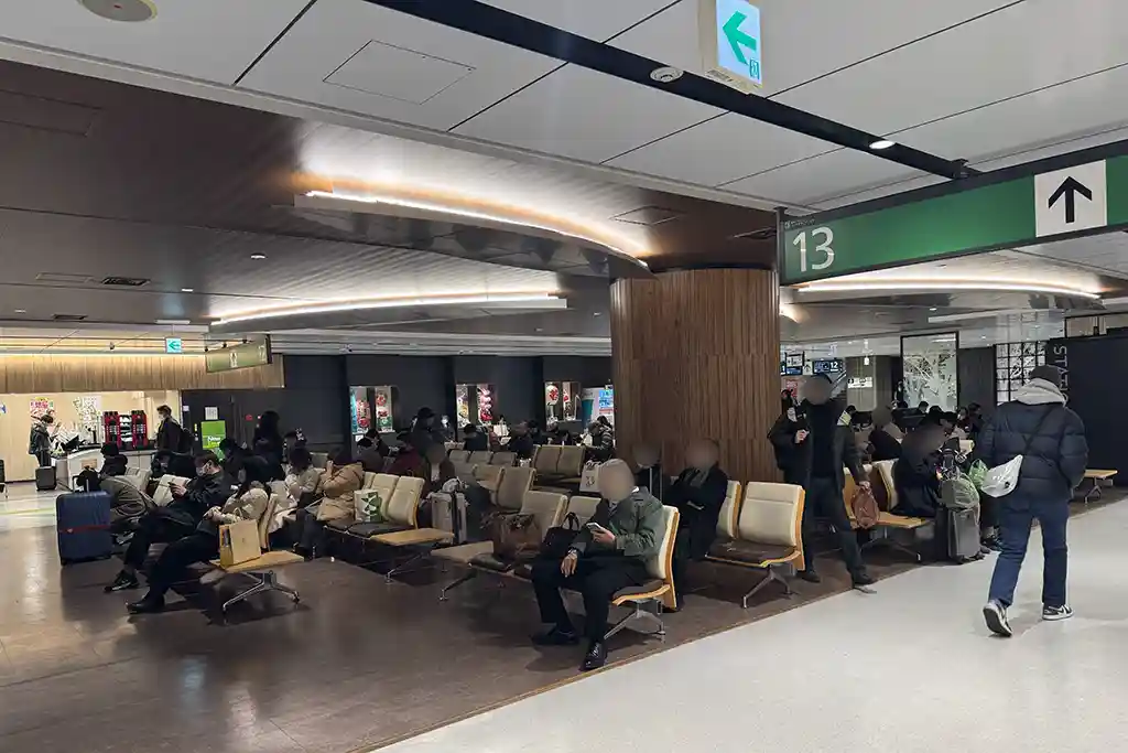 Spacious open seating area inside the Shinkansen zone at Sendai Station, where many passengers sit and wait.