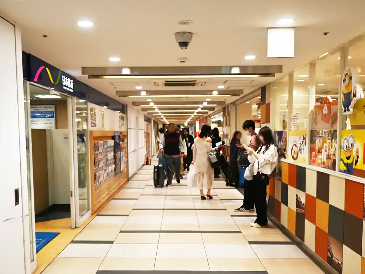 Corridor next to Nippon Travel shop at Shin-Osaka Station with passengers walking through shopping area