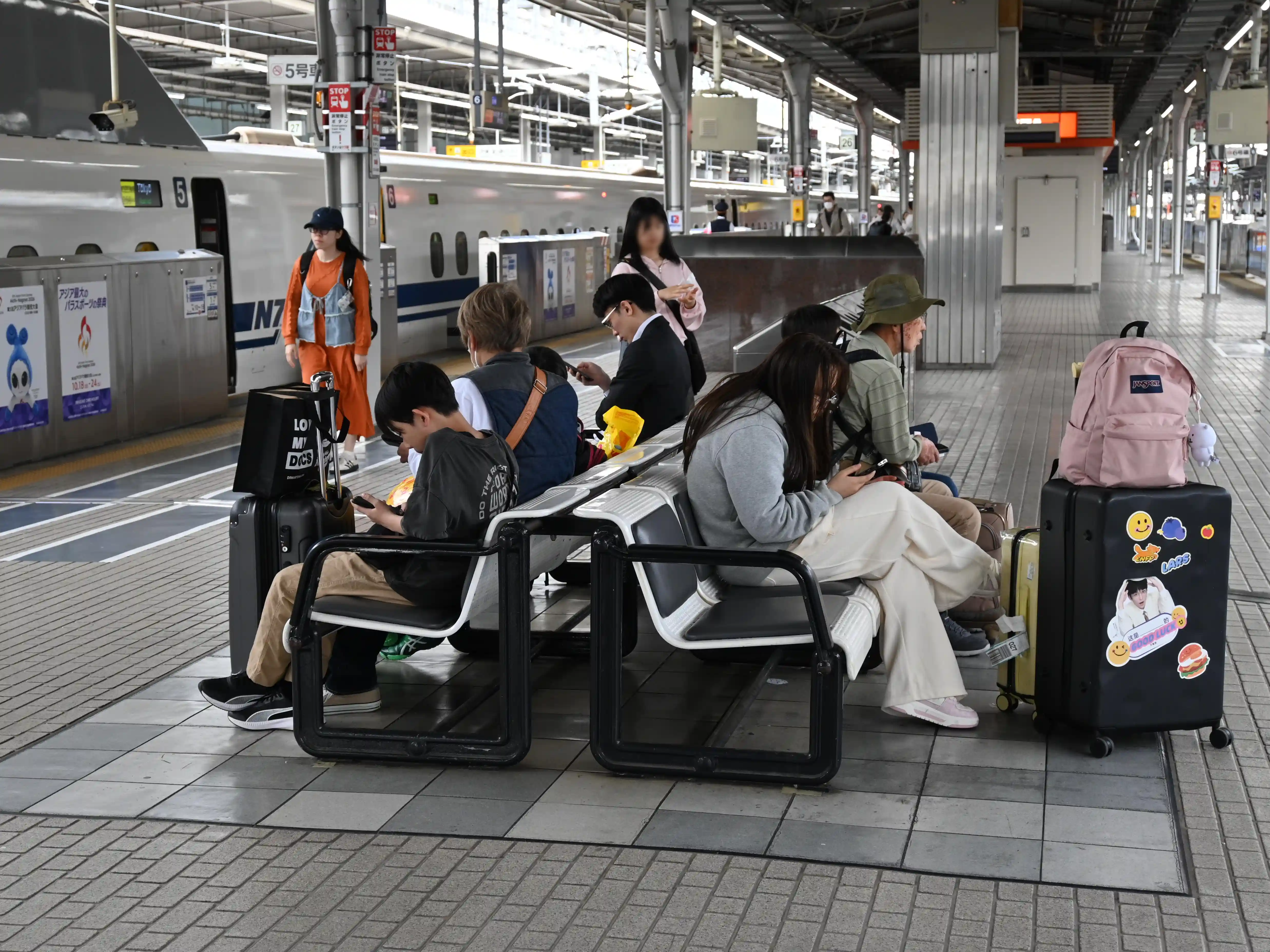 Passengers sitting on benches at Shin-Osaka Shinkansen platform waiting for the train