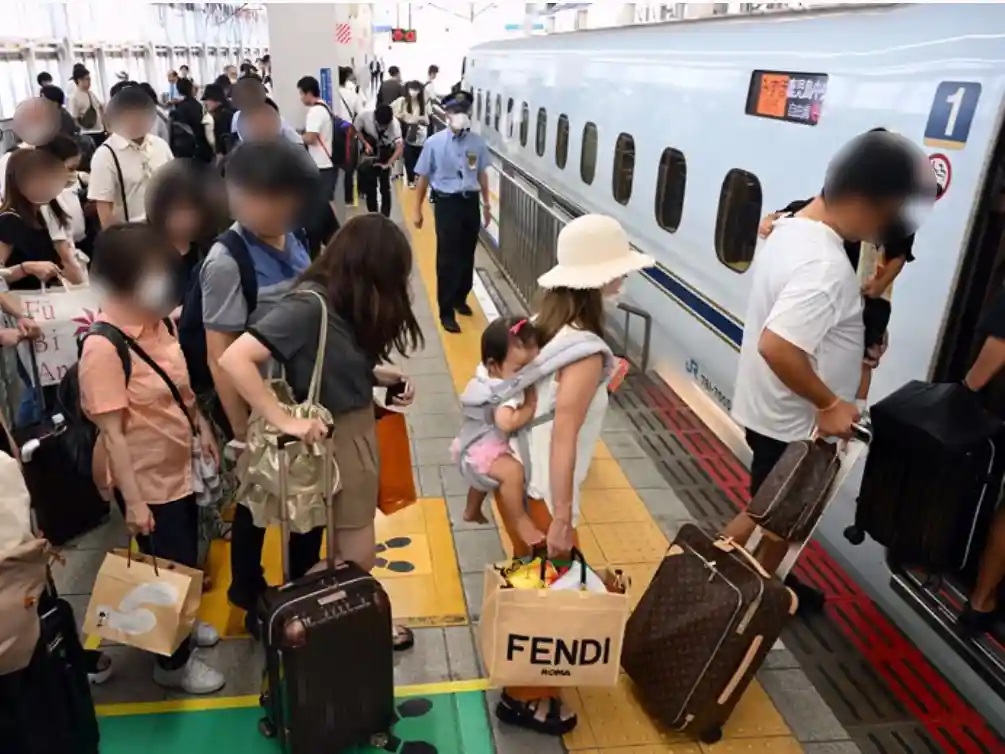 Passengers boarding a Shinkansen train at Hakata Station with luggage and boarding lines