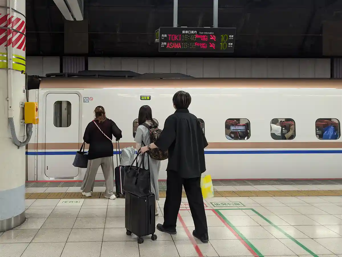Passengers with large luggage boarding a reserved Shinkansen car at Ueno Station platform