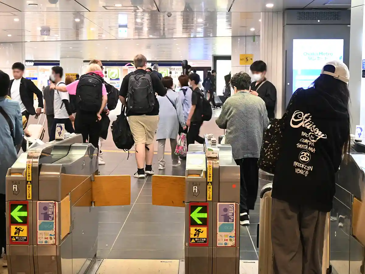 Passengers walking through Osaka Metro Midosuji Line ticket gates at Shin-Osaka Station concourse