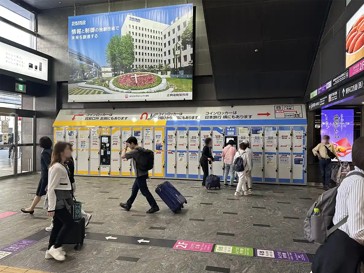 Coin lockers inside Hakata Station concourse with travelers storing luggage near the exits