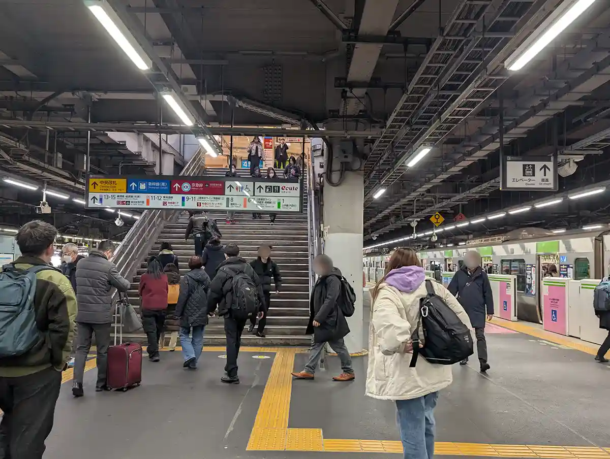 Yamanote Line platform at Shinagawa Station with passengers walking and stairs leading up to the concourse