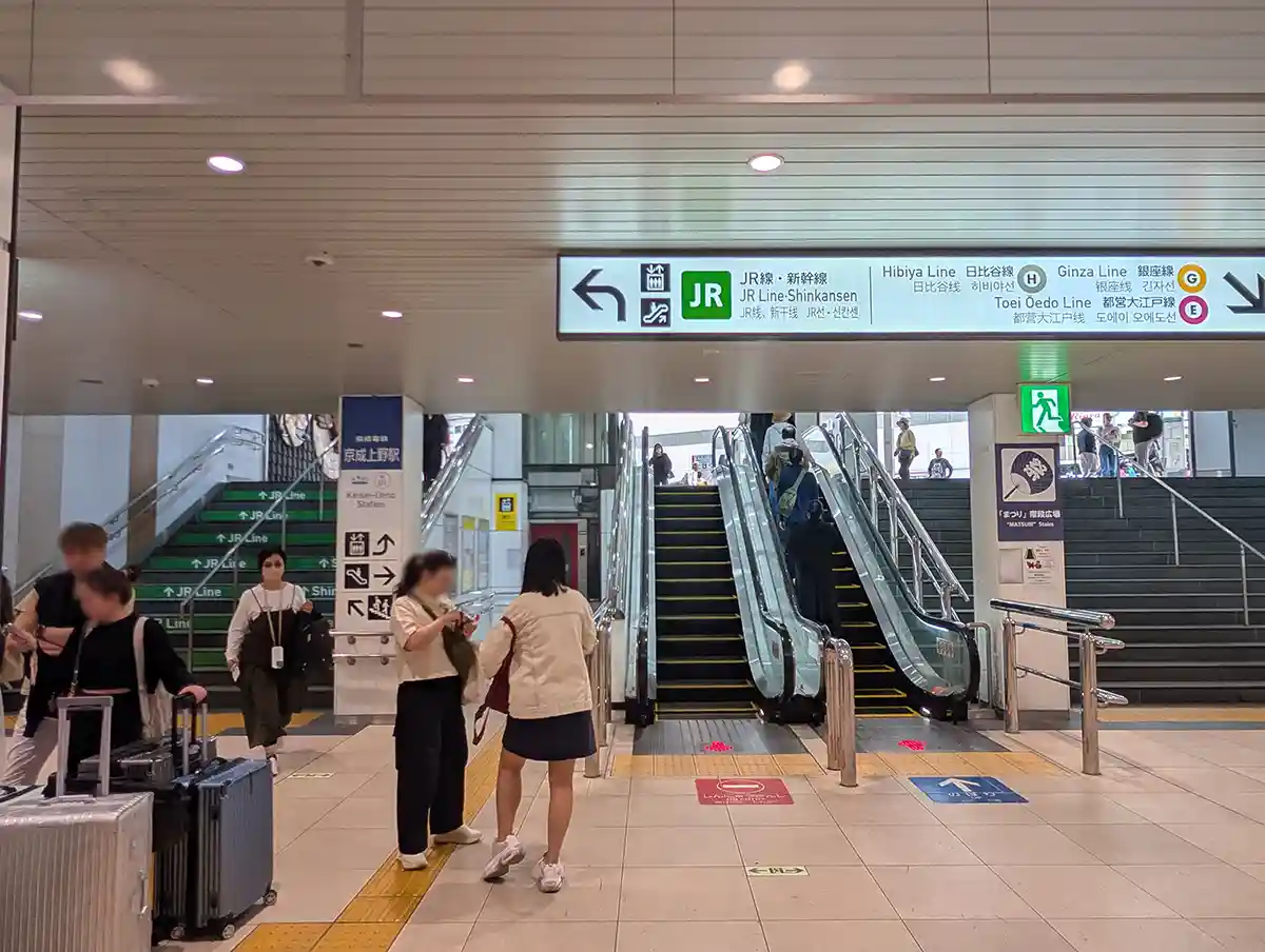 Keisei Ueno Station escalator with signs for JR Line, Shinkansen, and subway transfers