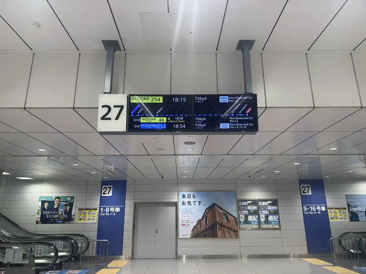 Departure board and car number signs at Shin-Osaka Shinkansen platform near escalator entrance