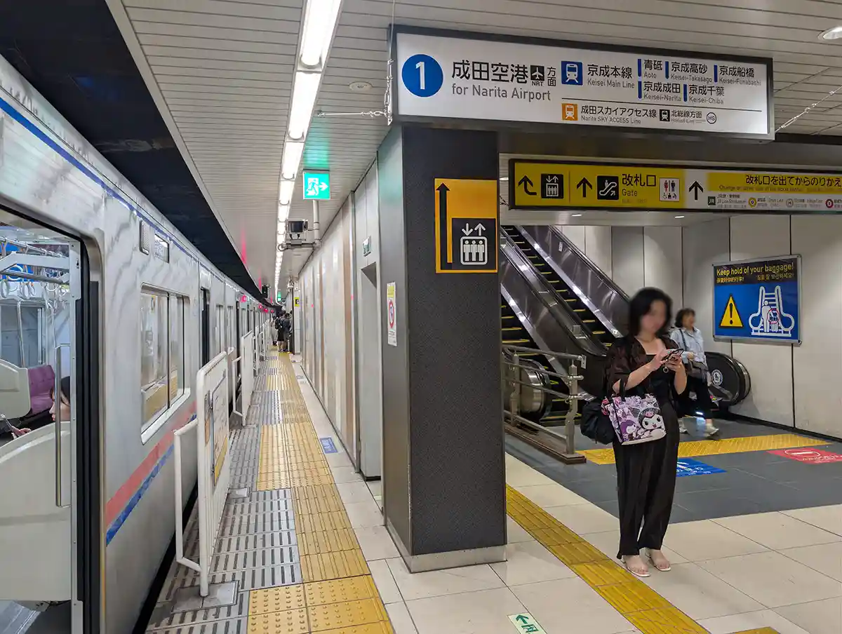 Keisei Ueno Station platform with a train, Narita Airport sign, and escalator nearby