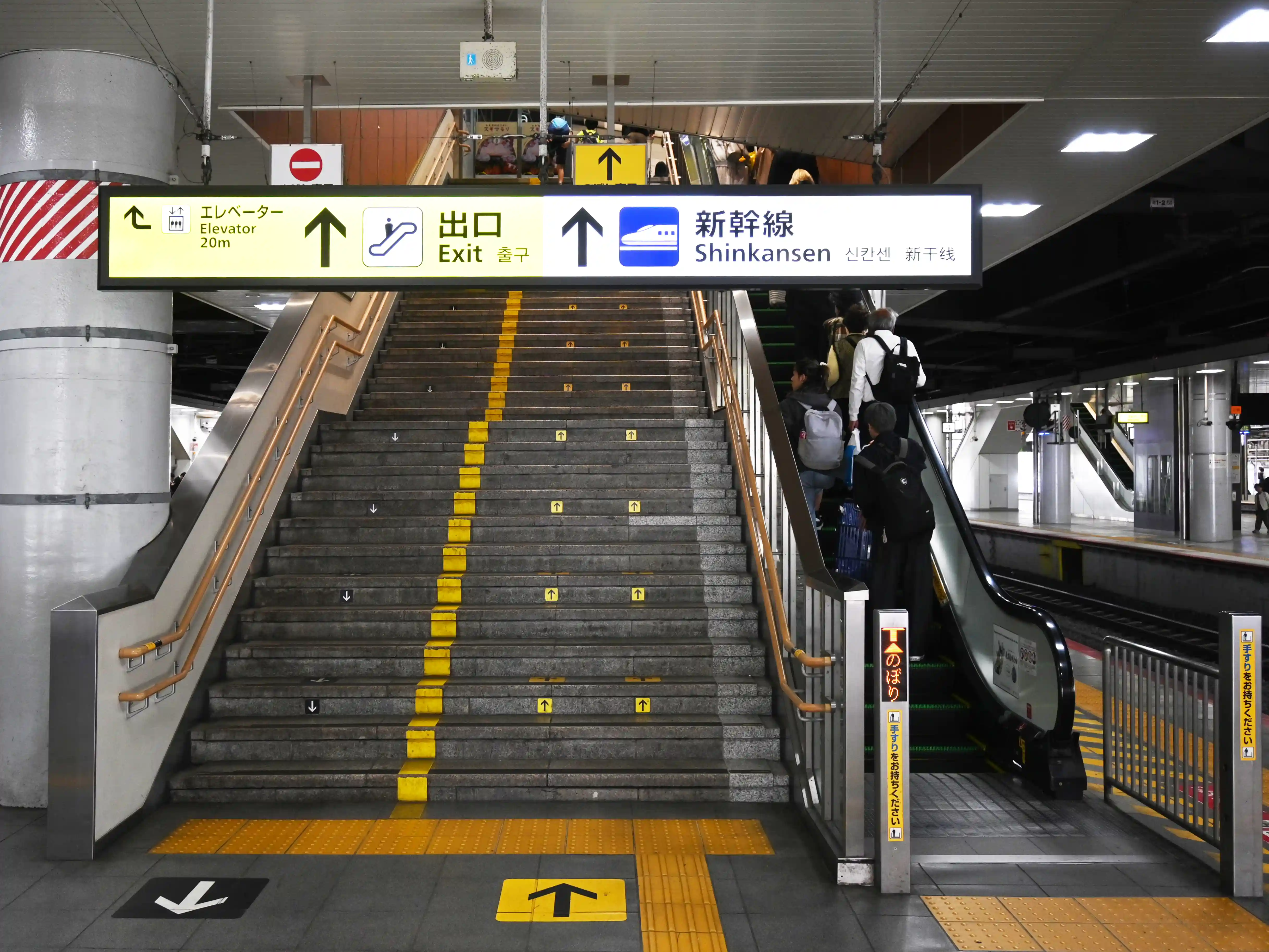 JR platform at Shin-Osaka Station with an escalator and sign pointing to Shinkansen and exit directions