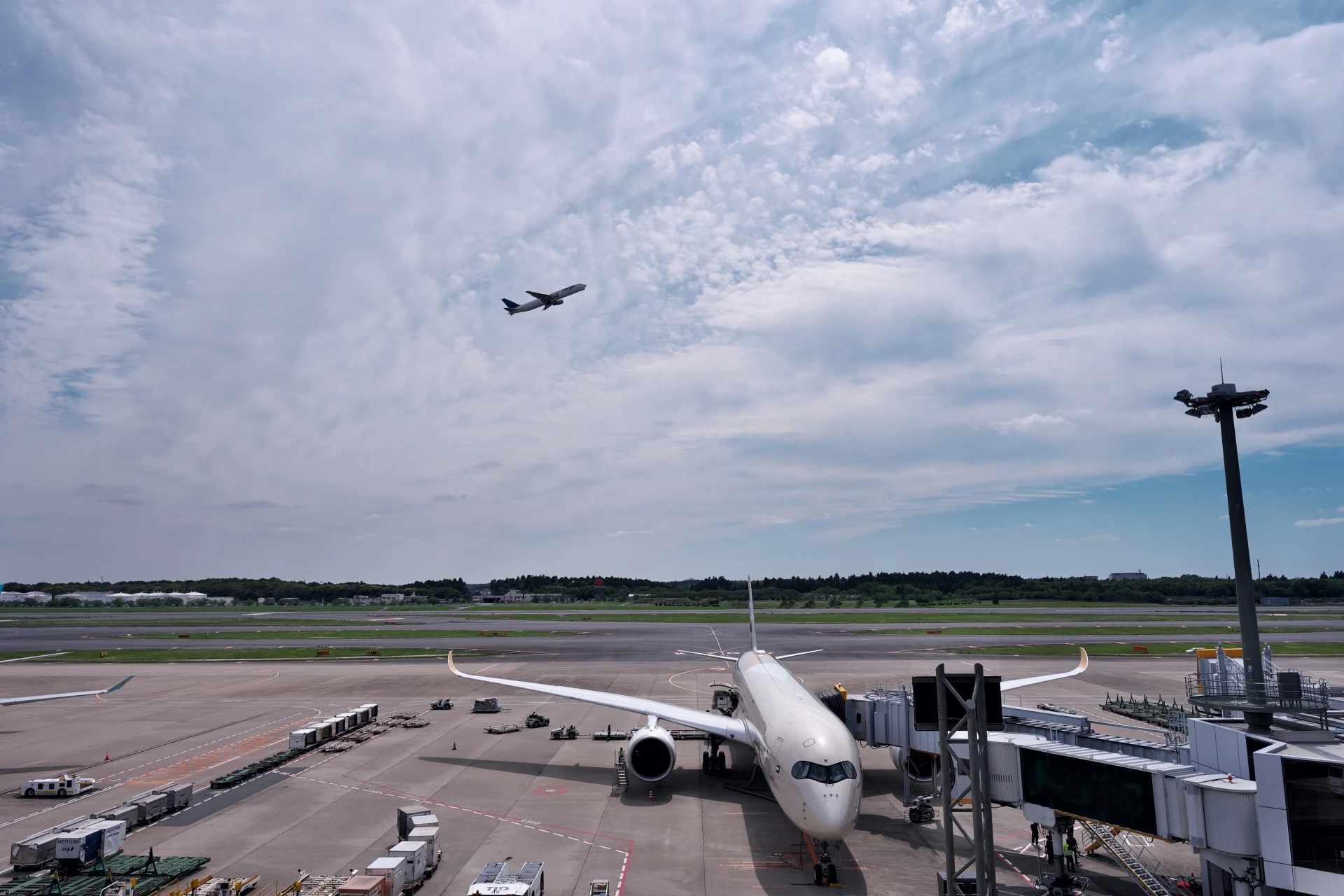 Narita Airport runway with airplanes at gate and one departing in the sky