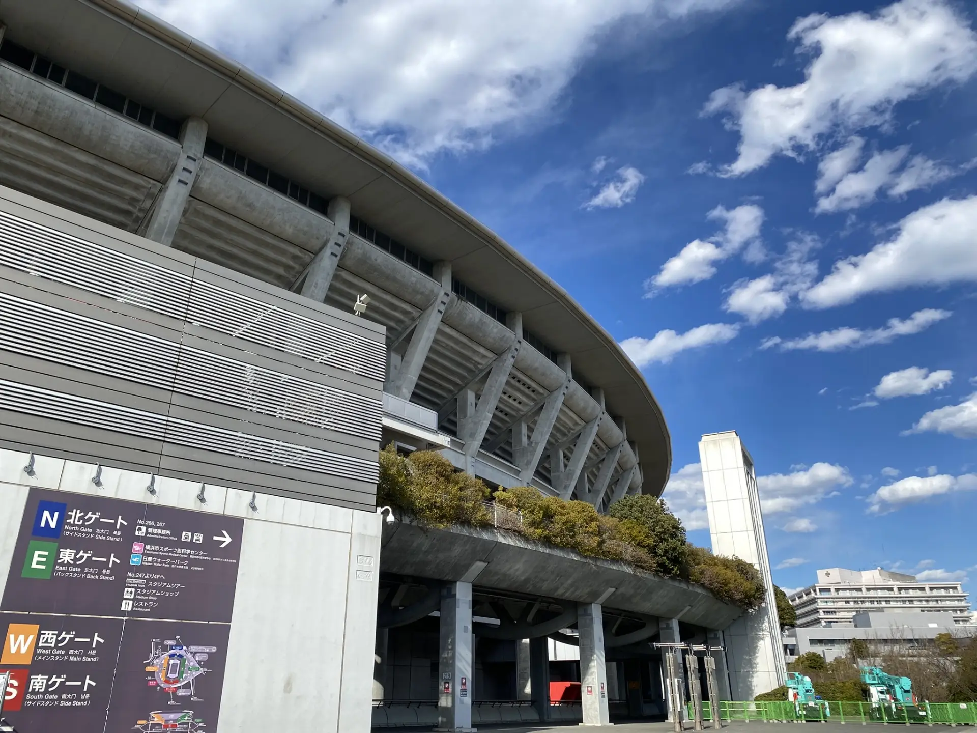 Exterior view of Nissan Stadium next to Shin‑Yokohama, with directional signs for main seating gates visible