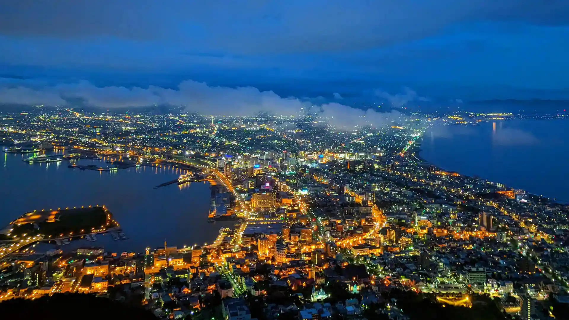 Nighttime view from Mount Hakodate overlooking Hakodate city, with dense urban lights and surrounding sea visible