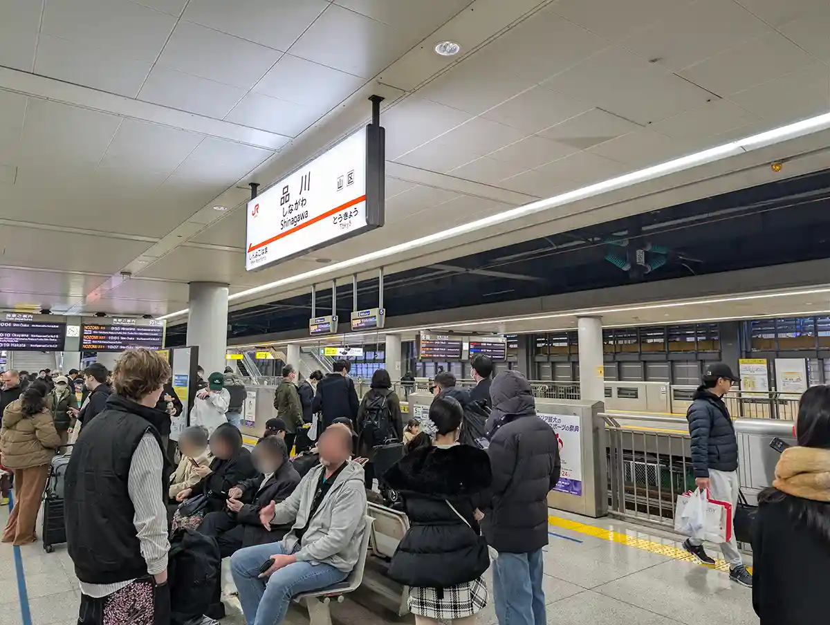 Shinkansen platform bench at Shinagawa Station with passengers waiting and departure boards in the background