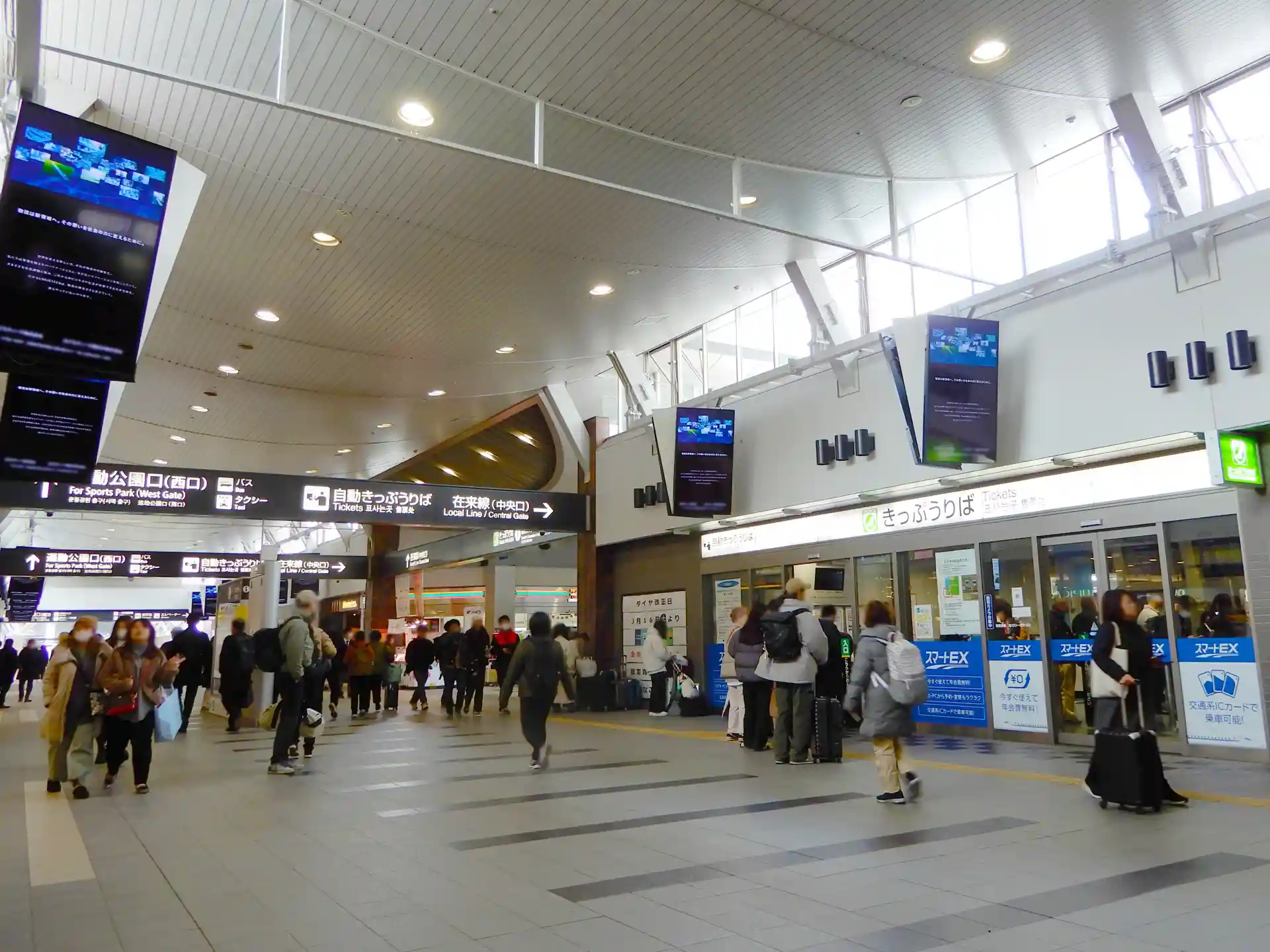 Indoor concourse at Okayama Station with direction signs guiding passengers to ticket gates and exits