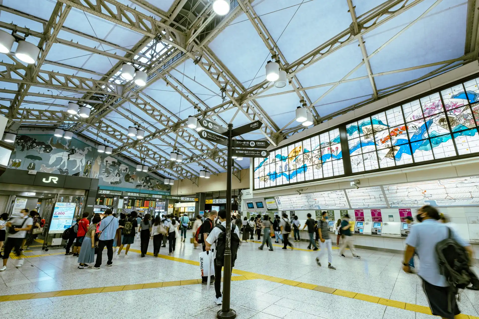 Travelers walking through the main concourse of Ueno Station with ticket machines and large mural art
