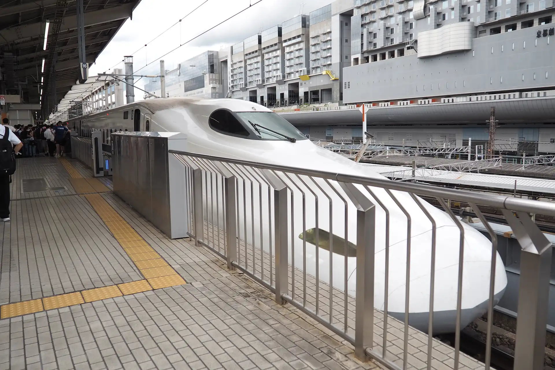 Shinkansen train at Kyoto Station platform with passengers waiting to board, showing the edge of the platform and station building in the background