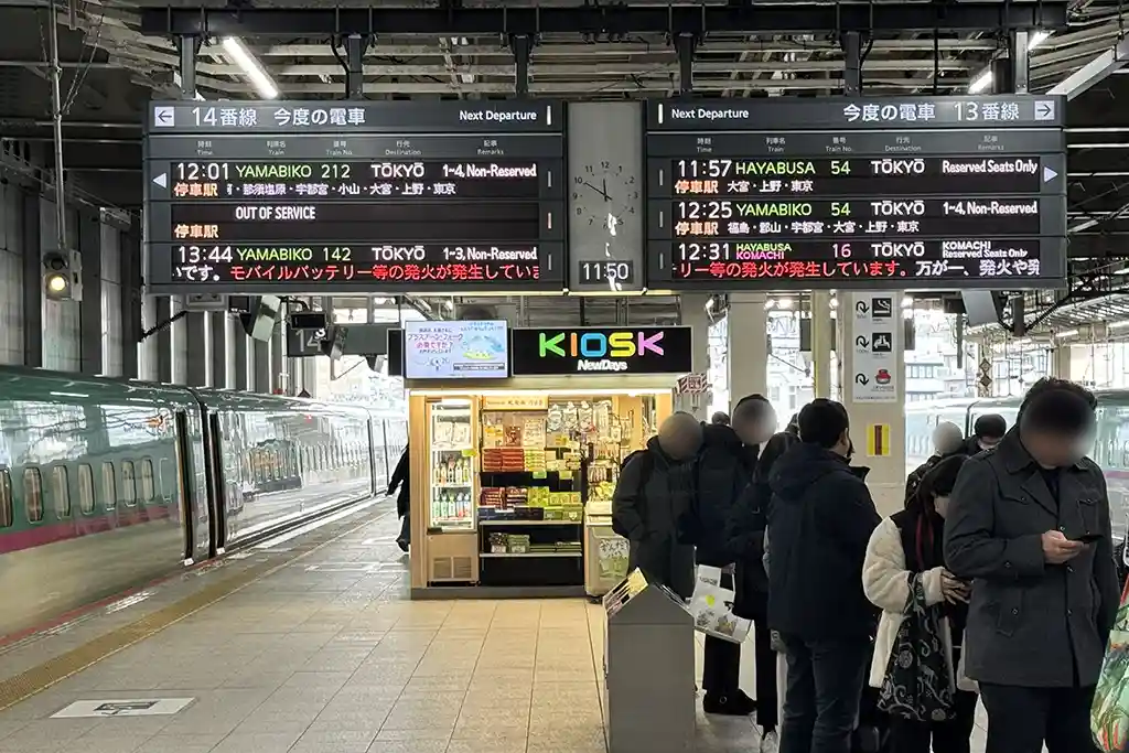 Shinkansen platform at Sendai Station displaying next departure information above passengers waiting to board.