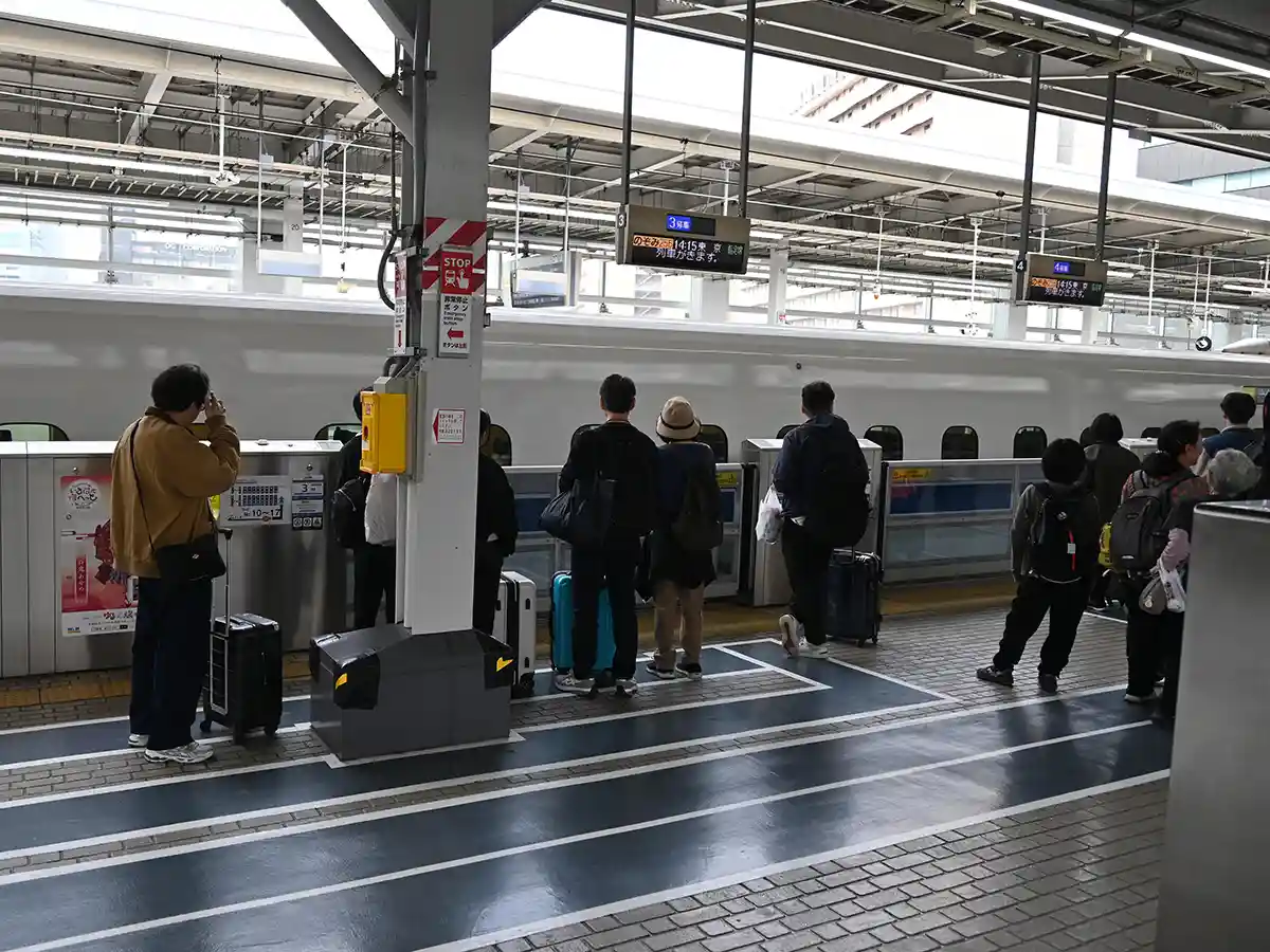 Passengers lining up behind safety yellow line on Shinkansen platform at Shin-Osaka Station waiting for train