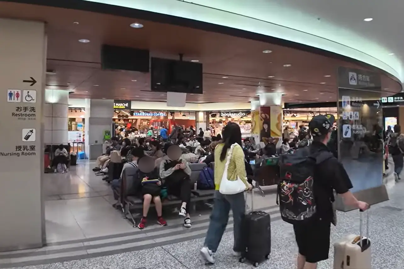 Rest space at Shin-Osaka Station where passengers are waiting with luggage, surrounded by shops and information signs