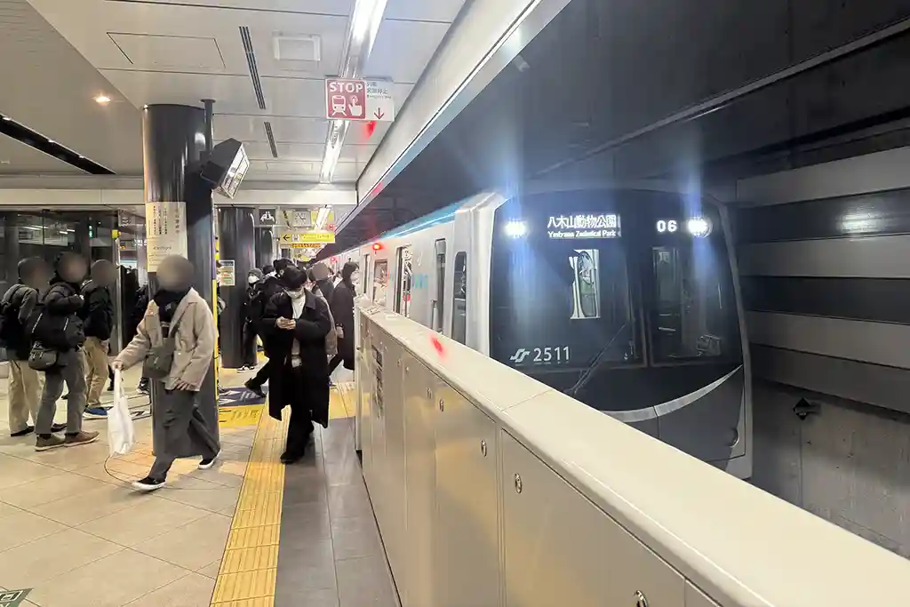 Sendai City Subway platform at Sendai Station with a train arriving and passengers standing nearby.