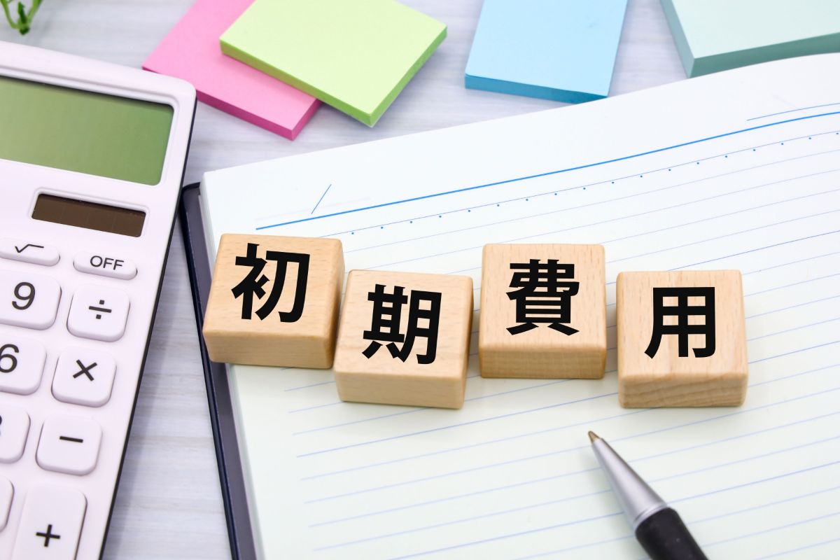 「初期費用」と書かれたウッドブロック、電卓、ノート、ペン。