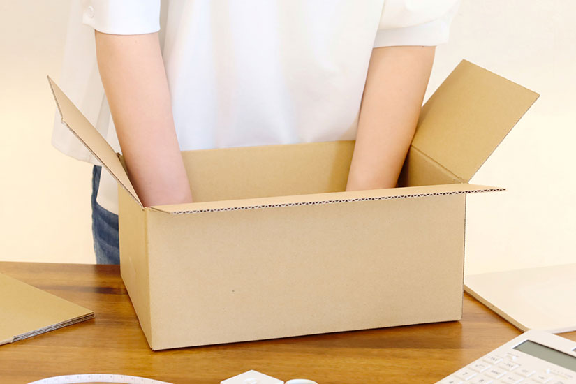 ダンボールの中に電卓やノートなどの日用品を梱包している写真