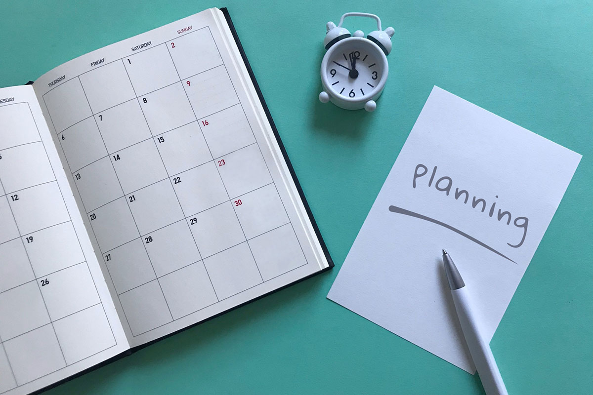 スケジュール帳と時計、プランニングと書かれた紙とボールペン。