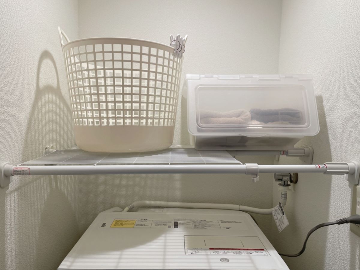 洗濯機上の突っ張り棚に置かれた、白い洗濯カゴとタオルが入った半透明の収納ケース。