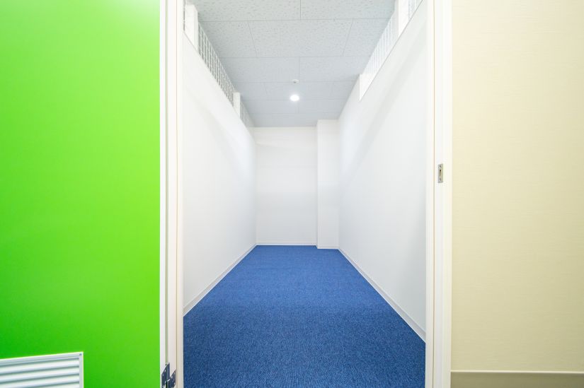 ストレージ王の屋内型トランクルームの画像。白い内壁と、青いカーペットが敷かれている。室内灯がついていて、トランクルームの室内も明るい。