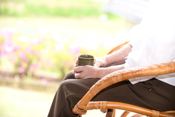 椅子に腰かけてお茶を飲む高齢者女性