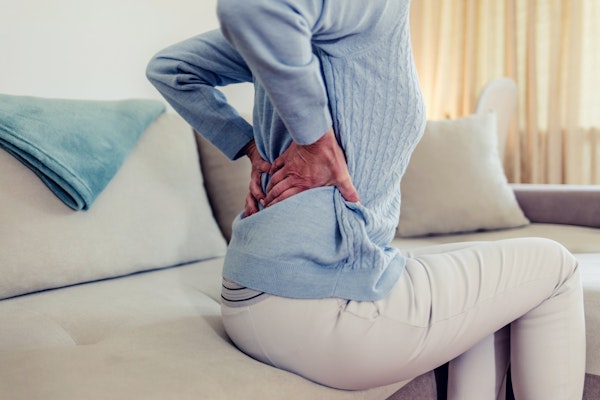 ソファで痛む腰を抑える女性