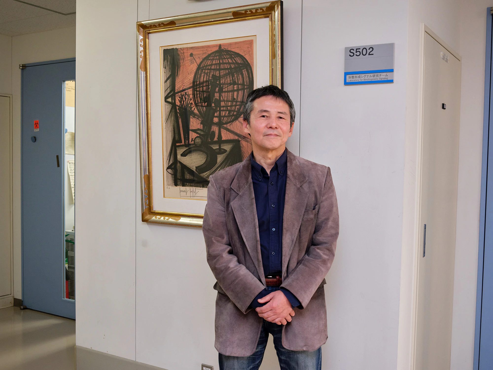 研究室の前でお気に入りの絵画と一緒に写る林先生
