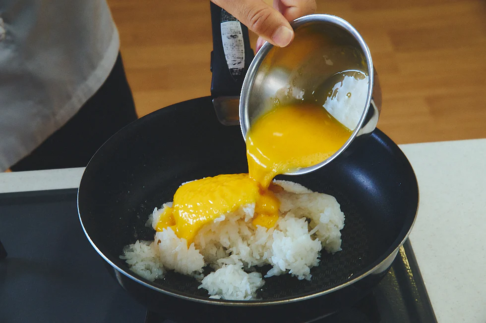 フライパンにご飯を入れ、その上にかき混ぜた卵を入れる様子