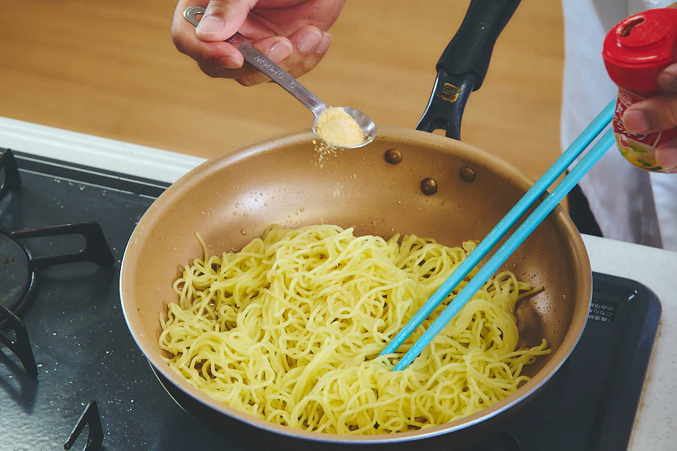 麺を炒めているフライパンの中に「丸鶏がらスープ™」を入れる様子